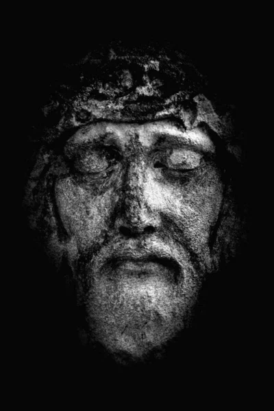 Close up antique stone statue Jesus Christ in a crown of thorns against black background as symbol of love, faith and religion.