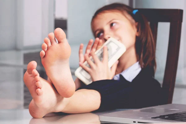 Portrait of very happy cute young business girl with bare feet on the table and counts money profit. Selective focus on feet