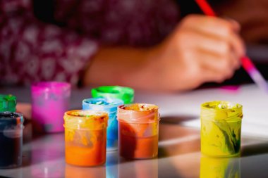 Suluboya resim yapmayı öğrenen genç bir kızın portresi yok. Renkli fırçalar kullanarak evde çizim yapıyor. Boyalı tüplere odaklan..