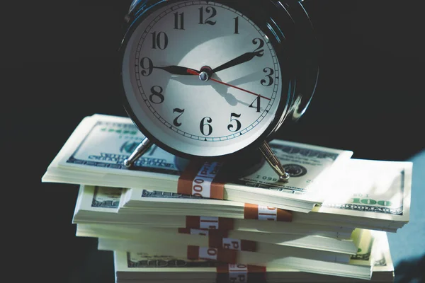 Conceptual image: Time value of money. Alarm clock and US Dollar packs on black background..