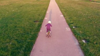 Boy On Bike with protective helmet learning to Ride In City Park At Spring Day Sunset