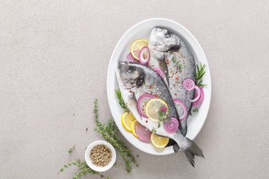 Taze dorada balığı ve pişirmek için malzemeler. Beyaz arka planda baharatları olan çiğ deniz çipurası. Sağlıklı yiyecekler, diyet. Kopyalama alanı olan üst görünüm.