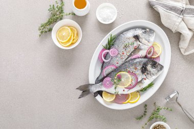 Taze dorada balığı ve pişirmek için malzemeler. Beyaz arka planda baharatları olan çiğ deniz çipurası. Sağlıklı yiyecekler, diyet. Kopyalama alanı olan üst görünüm.