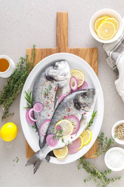 Taze dorada balığı ve pişirmek için malzemeler. Beyaz arka planda baharatları olan çiğ deniz çipurası. Sağlıklı yiyecekler, diyet. Kopyalama alanı olan üst görünüm.