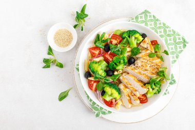 Öğle yemeğinde brokoli, domates, soğan, zeytin, mısır salatası ve ızgara tavuk göğsü ile makarna kasesi. Sağlıklı beslenme. Üst görünüm.