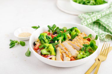 Öğle yemeğinde brokoli, domates, soğan, zeytin, mısır salatası ve ızgara tavuk göğsü ile makarna kasesi. Sağlıklı beslenme.