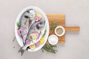 Taze dorada balığı ve pişirmek için malzemeler. Beyaz arka planda baharatları olan çiğ deniz çipurası. Sağlıklı yiyecekler, diyet. Kopyalama alanı olan üst görünüm.