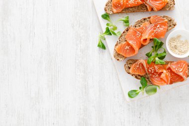 Beyaz rustik ahşap bir masada tuzlanmış somon balıklı tam tahıllı çavdar ekmekli sandviç. Sağlıklı yiyecekler. Üst görünüm