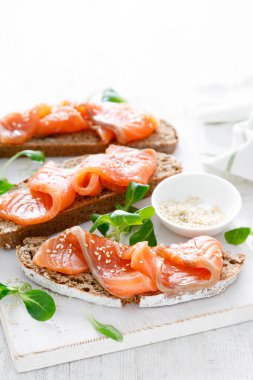 Beyaz rustik ahşap bir masada tuzlanmış somon balıklı tam tahıllı çavdar ekmekli sandviç. Sağlıklı yemek.