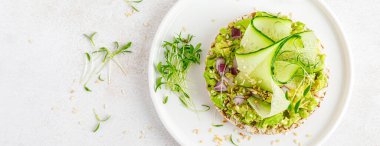 Vegan open sandwich with dietary crispbread, fresh cucumber, onion, sesame seed, microgreens and avocado. Healthy vegetarian food, diet. Top view. Banner.
