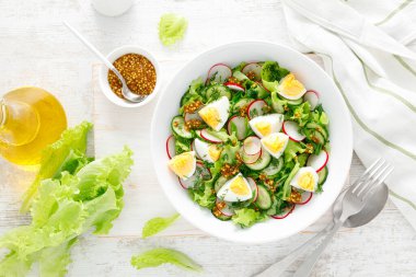 Paskalya taze sebze salatası haşlanmış yumurta, turp ve salatalık, dijon hardallı sos ve limonlu beyaz ahşap masa. Üst görünüm