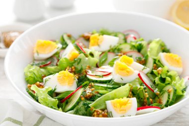 Paskalya taze sebze salatası haşlanmış yumurta, turp ve salatalık, dijon hardallı sos ve beyaz ahşap masada limon.