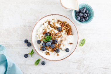 Bir kase taze yaban mersinli granola, süzme peynir veya kaymak, yoğurt ve fındık. Sağlıklı yiyecekler. Kahvaltıda. Üst görünüm