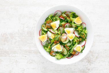 Paskalya taze sebze salatası haşlanmış yumurta, turp ve salatalık, dijon hardallı sos ve limonlu beyaz ahşap masa. Üst görünüm