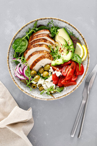 Grilled chicken breast and fresh vegetable salad with tomatoes, feta cheese, olives and avocado. Healthy food. Top view