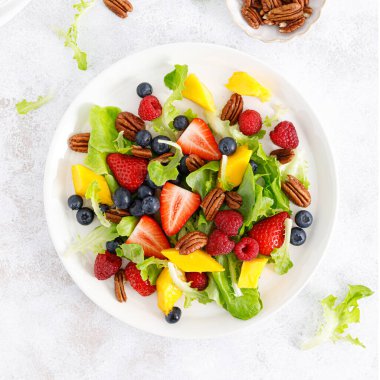 Çilekli, böğürtlenli, ahududulu, mangolu ve cevizli meyve salatası. Sağlıklı yiyecekler, diyet. Üst görünüm