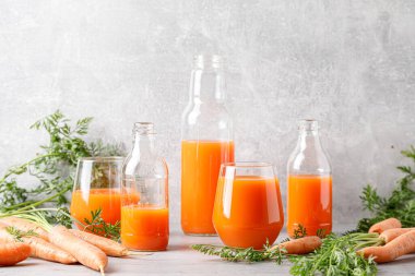 Carrot juice in a glass and bottle and fresh carrots with leaves