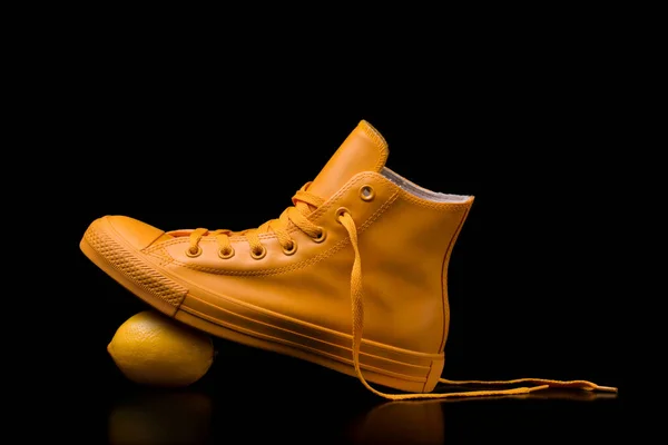 黄色的运动鞋踩在柠檬上 衬托着黑色的背景 免版税图库图片
