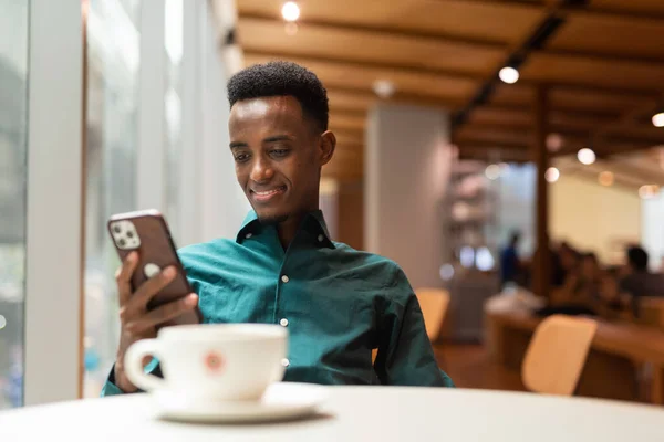 Handsome young black man in coffee shop using phone