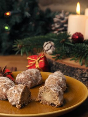 Lezzetli bir Noel çelengi, Noel süslemeleri ve mevsimlik yiyeceklerin önünde seramik bir tabakta çalınmış.