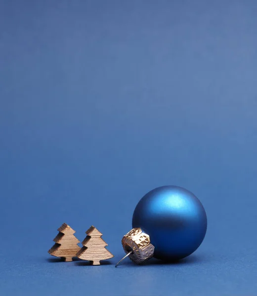 Niebieska Piłka Choinkowa Małymi Drewnianymi Kształtami Drzew Niebieskim Papierowym Tle — Zdjęcie stockowe