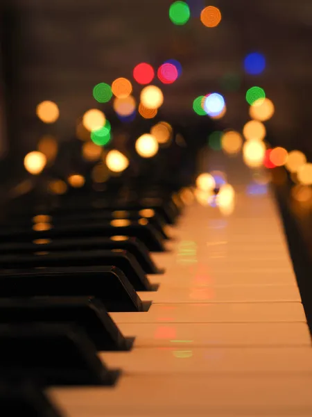 妖精の光とカラフルなぼやけたクリスマスライトとピアノのキーボード 季節の背景 — ストック写真
