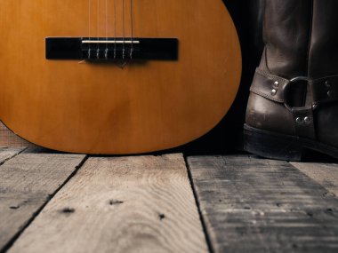 Ahşap ahşap üzerinde akustik gitarı olan eski kovboy çizmeleri.