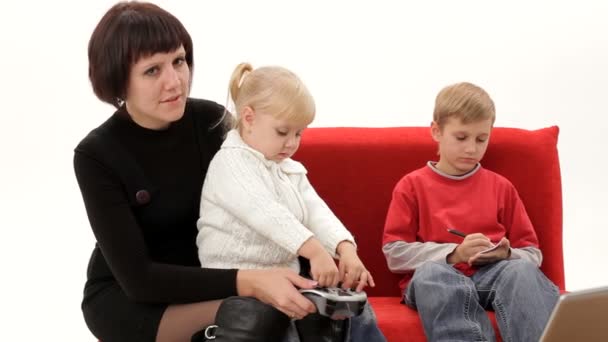 Mãe e filha jogando videogames, filho escreve em um caderno — Vídeo de Stock
