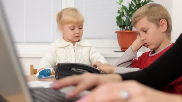 Ensamstående mamma. två små barn spelade medan deras mamma jobbar hårt på den bärbara datorn. Motion zoom — Stockvideo