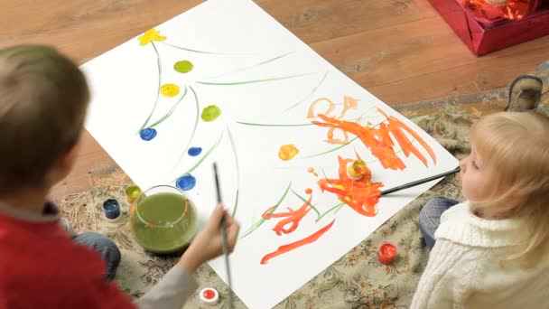 Los niños pintan sobre lienzo. Dos niños pequeños sentados en el suelo y pintando un árbol de Navidad . — Vídeos de Stock