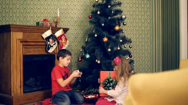 Les enfants cherchent leurs cadeaux sous un arbre de Noël, puis se cachent. Cadeaux sous un sapin de Noël . — Video