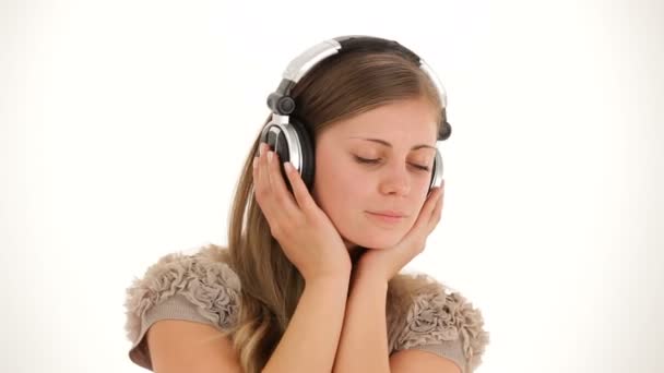 Música en los auriculares. Una chica con una camisa blanca y auriculares bailando sobre un fondo blanco. Dos cuadros . — Vídeo de stock