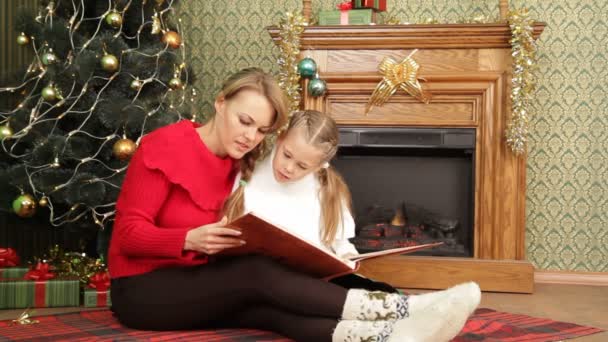 Moeder lezen een verhaal aan haar dochter onder een kerstboom. lezen van een verhaal. — Stockvideo