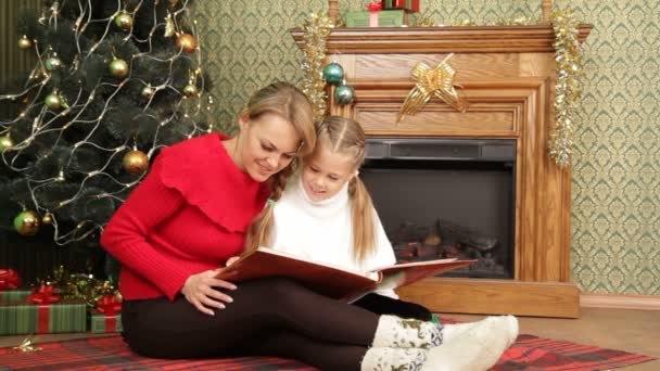 Madre leyéndole un cuento a su hija bajo un árbol de Navidad. Leer una historia . — Vídeos de Stock