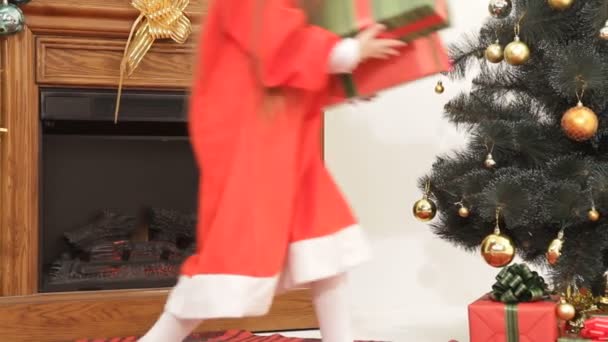 Flicka lägger julklappar under en julgran. — Stockvideo