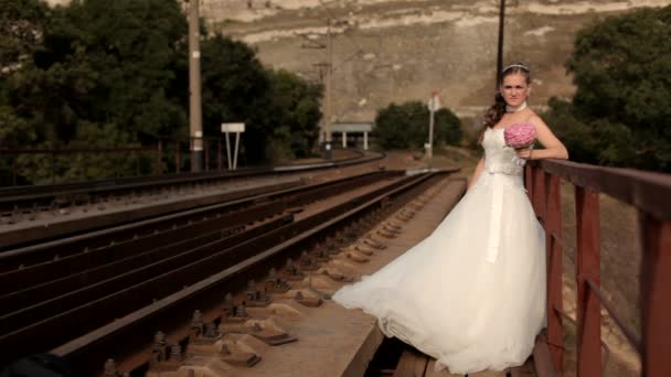 La esposa espera en los rieles. Hermosa mujer en un vestido de novia se para en el ferrocarril . — Vídeo de stock