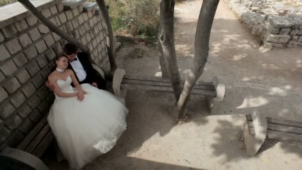 Romance dans le parc. Jeunes mariés assis sur le banc et étreignant . — Video