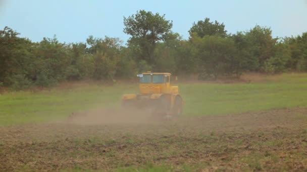 A large farm tractor plowed land. Behind the tractor heaves a big cloud of dust. Tracking shot. — Stock Video