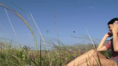 bir kız kulaklık ile müzik dinler. güzel genç kız üzerinde yeşil bir alana oturan ve büyük kulaklık aracılığıyla müzik dinlemek. hareketli kamera.