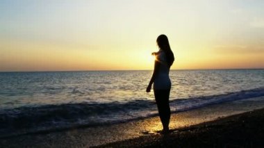 Denizde gün batımı. Bir kız sahilde durup gün batımını izliyor. Dalgalar ayaklarını yıkar..