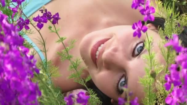 Schönes Mädchen liegt zwischen Lupinen. sie liegt auf dem Feld zwischen wunderschönen lila Blumen. — Stockvideo