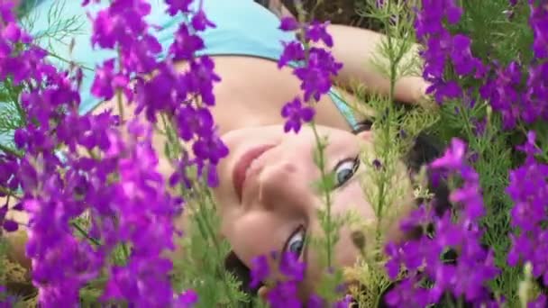 Beautiful girl lies among lupine. She lies on the field among beautiful purple flowers. — Stock Video