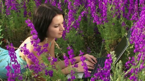 Dívka ležela s notebookem. dívka leží na poli krásných květin a vyškoleni na laptop. — Stock video