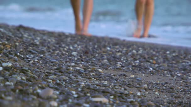 Περπατώντας κατά μήκος της ακτής. δύο κορίτσια να βγουν στην παραλία όπως τα κύματα πλένουν τα πόδια τους. — Αρχείο Βίντεο
