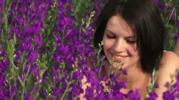 Flickan är bland den lila blommor unga flickan liggande på ett vackert fält av lila blommor och leenden. — Stockvideo