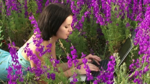 La chica estaba acostada con el portátil. Chica acostada en el campo de hermosas flores y entrenada en el portátil . — Vídeos de Stock