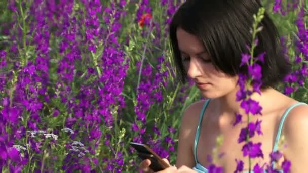 Girl wrote a message. Beautiful girl gaining SMS message on her mobile phone in the midst of lupine. — Stock Video