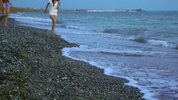 Chicas en la orilla. Dos chicas en la playa. Una chica corre a las orillas de la distancia segunda chica va lentamente. Las olas lavan sus pies . — Vídeos de Stock