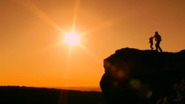 Sole. Silhouette. Un uomo con un bambino si avvicina al bordo della scogliera. Poi alzarono entusiasticamente le mani . — Video Stock