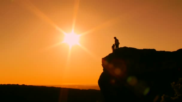 Cielo soleggiato. Silhouette. Un uomo con un bambino sul ciglio della scogliera. Poi alzarono entusiasticamente le mani . — Video Stock